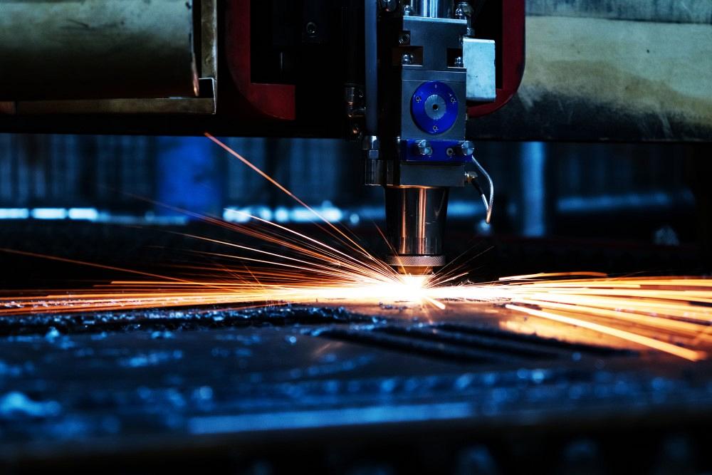 The laser machine cuts a metal sheet and bright sparks fly out of its work. Laser machine at a metalworking factory.