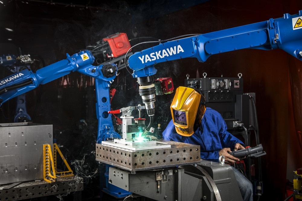 A human welder works with a robot