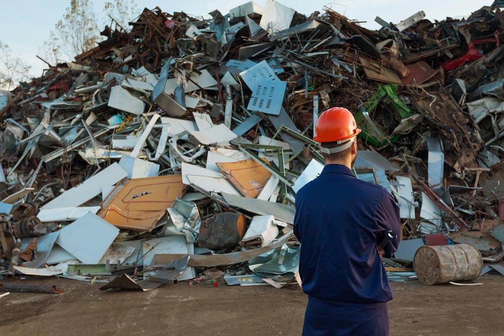 worker standing in front of pile of disposed objects in recycling center