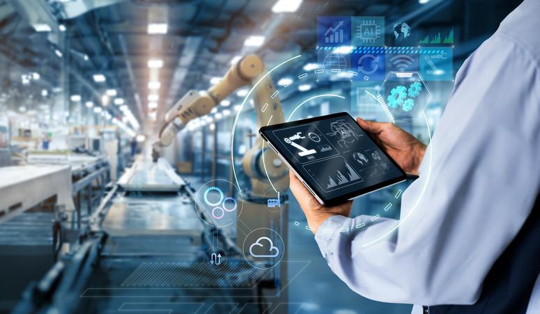 A man holds a tablet as he looks over automated machinery.