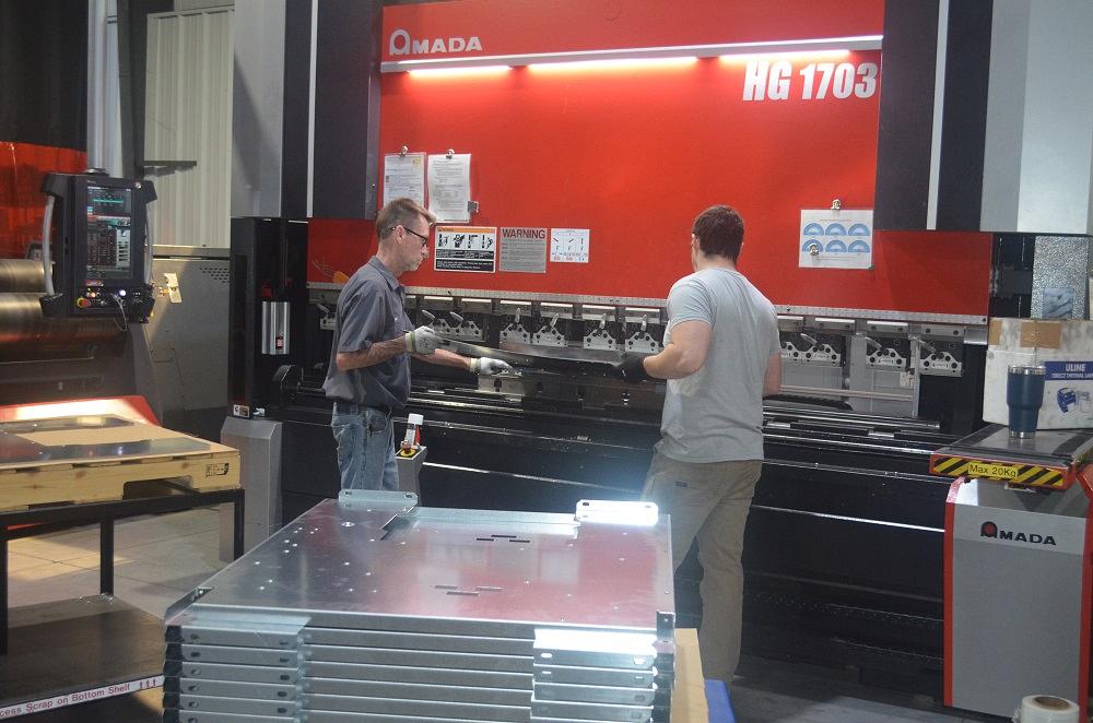 Two operators hold a part being formed on a press brake.