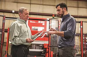 Two men inspect a metal part.