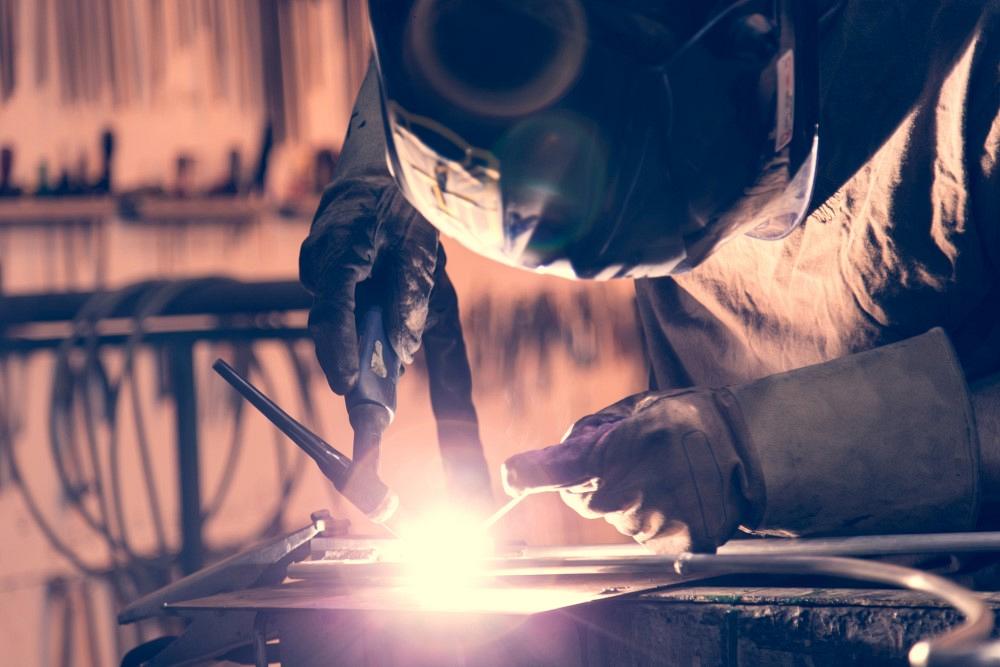 A man using a TIG (Tungsten Inert Gas) welder in a workshop.