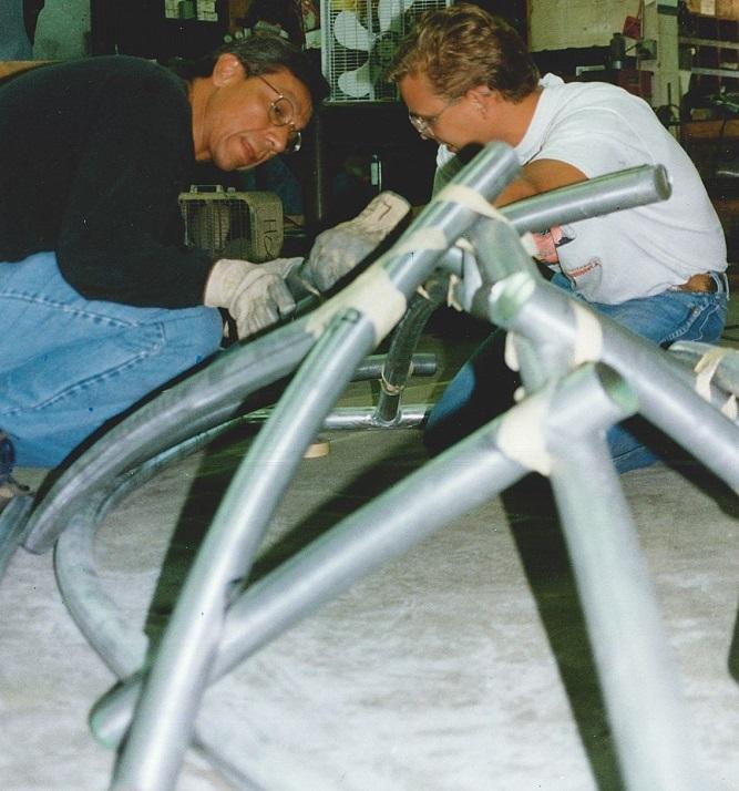 Two men build a structure of aluminum rods.