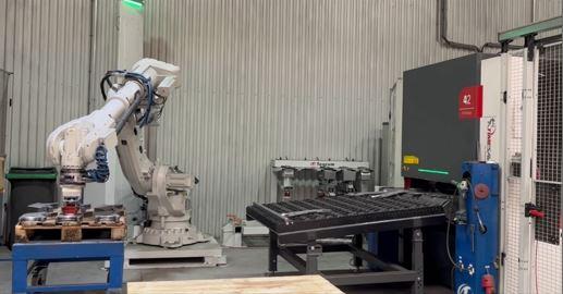 A robot loads parts onto a conveyor feeding a deburring machine.