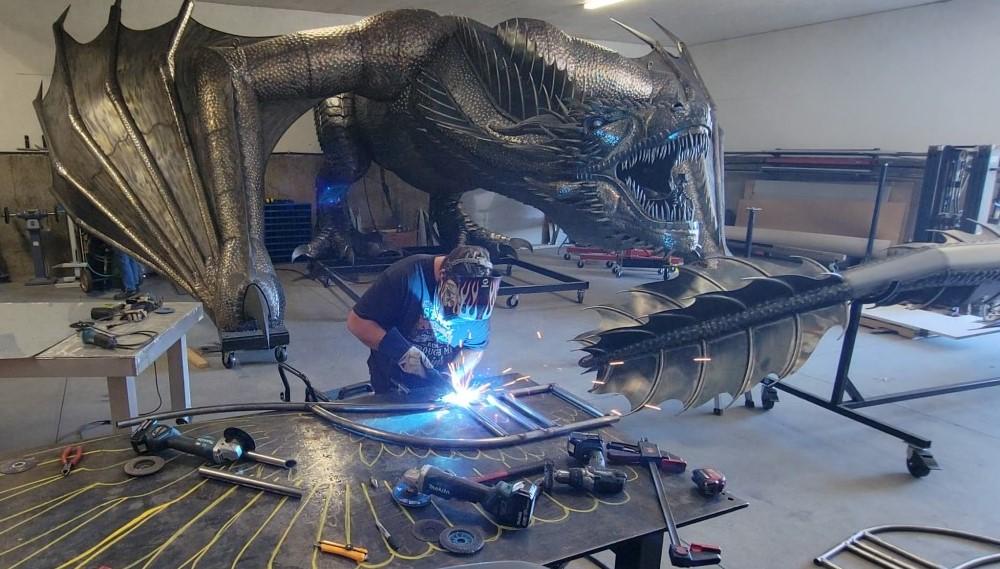 Metalen kunstbeeldhouwer en kunstenaar met een metalen sculptuur van een draak