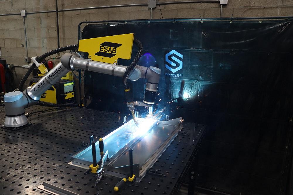 A cobot attached to a welding table is shown in action.