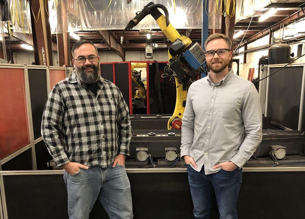 Two men stand in front of a robot.