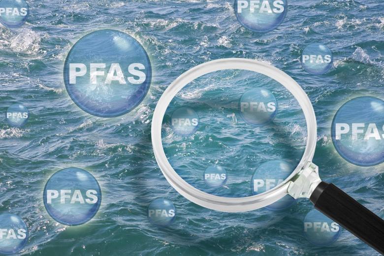A magnifying glass looks at PFAS particles in water.