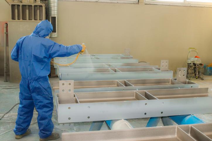 A worker sprays a cleaner on metal parts.