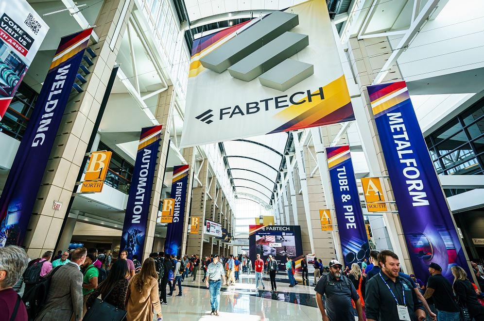 People walk on the FABTECH show floor among colorful banners.