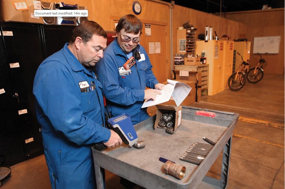 Two people inspect a metal part.