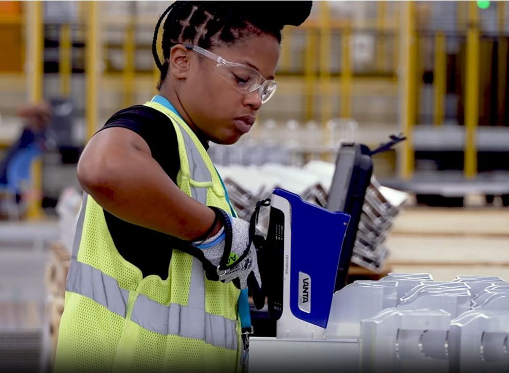 A woman uses an analyzer tool to verify material composition of a part.