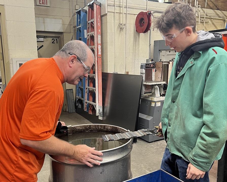 A teacher and student examine a welded metal part.