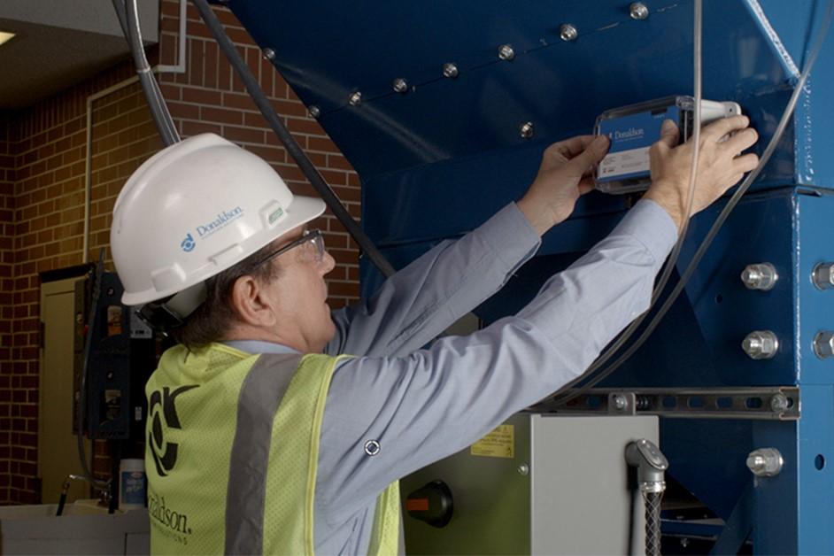 A technician installs remote monitoring equipment on a dust collector.