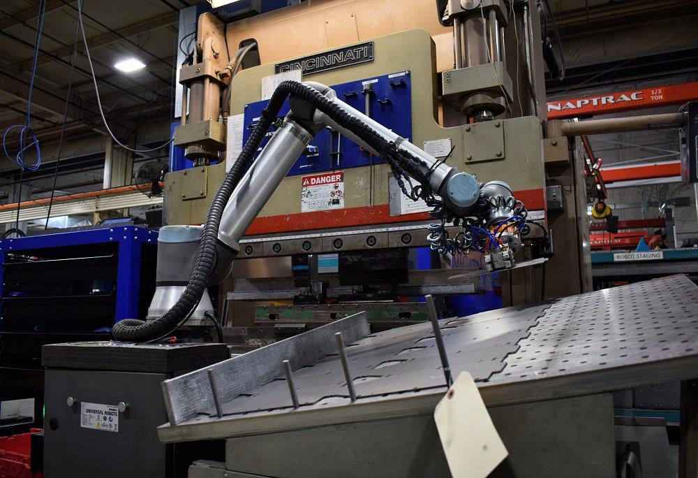 A collaborative robot delivers a part to an older press brake.