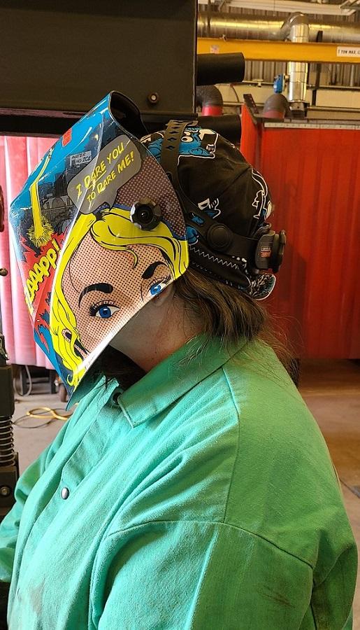 A student wearing a welding helmet welds.
