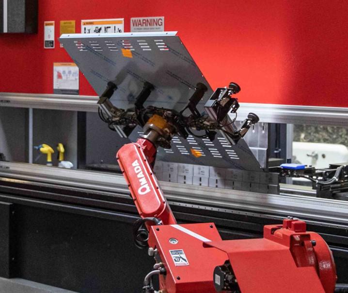 A robot holds a metal piece being bent in a press brake.