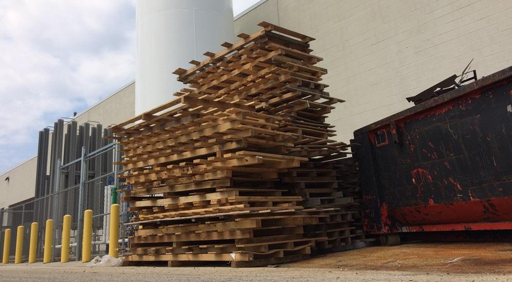 Wooden pallets are stacked on each other behind a manufacturing plant.
