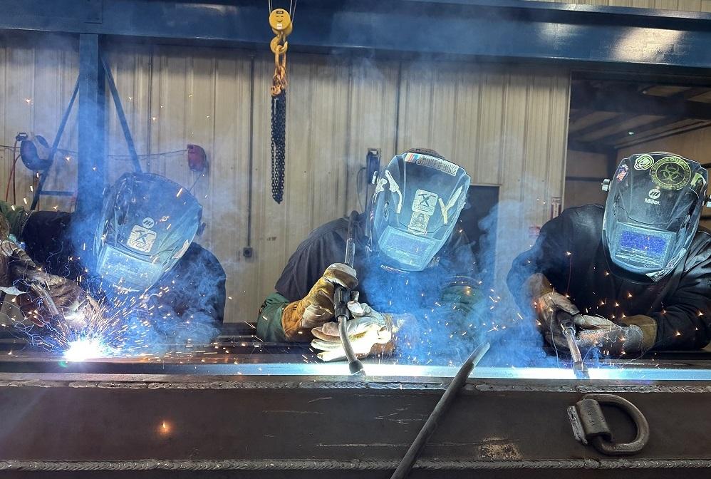 Three workers perform MIG welding.