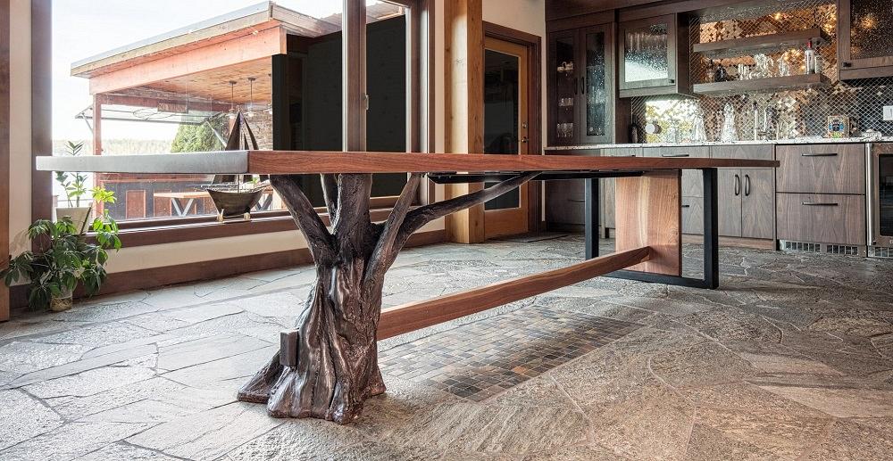 A walnut-topped dining room table is supported by metal legs sculpted line tree branches.