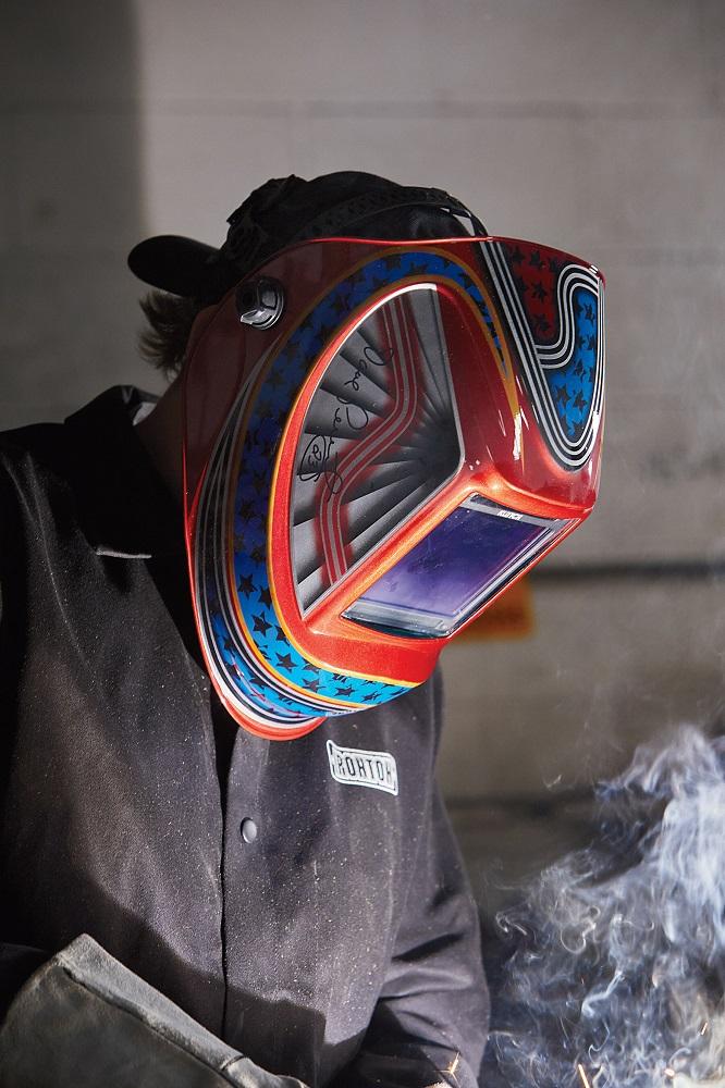 A welder wears a colorful welding helmet.