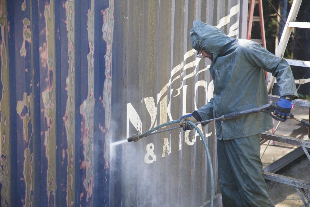 Using a wet sandblaster to remove rust from steel shipping container
