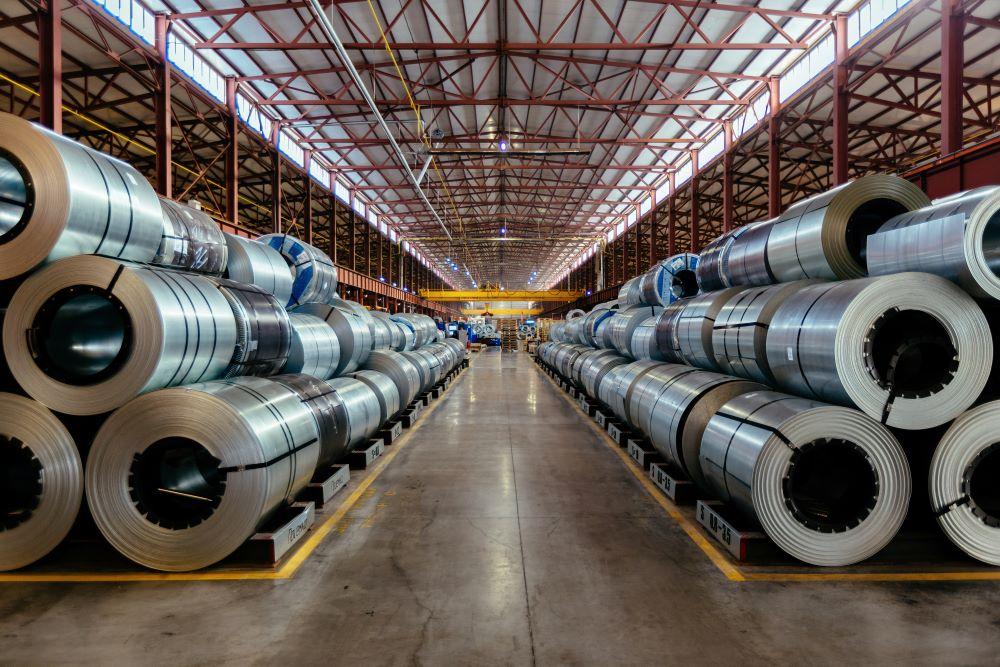 Rolls of galvanized steel sheet sit in racks in a warehouse.