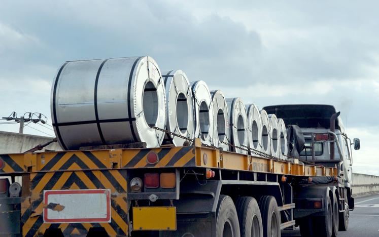 A truck with a flat-bed trailer delivers steel coils.