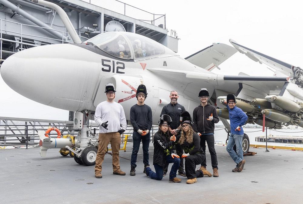 People pose in front of a fighter jet.