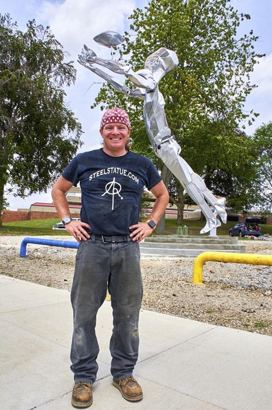 A man stands in front of a metal sculpture of a football player.