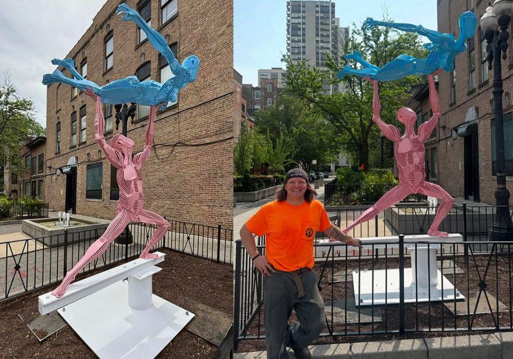 A pink and blue metal sculpture shows a person lifting another person overhead.