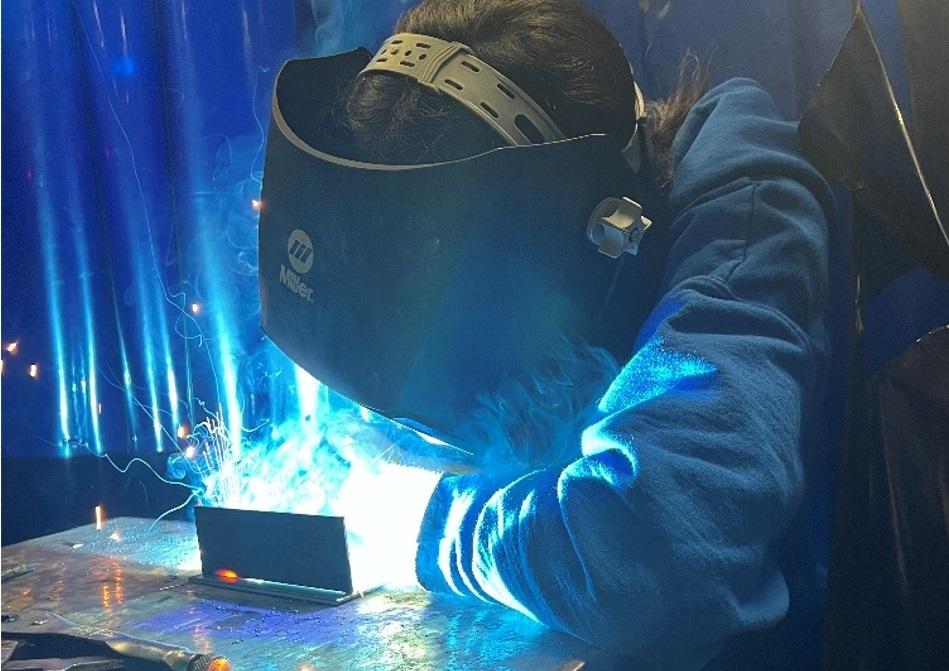 A girl welds two pieces of metal together.