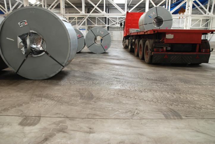 Steel coils are loaded onto a flat-bed trailer in a warehouse.