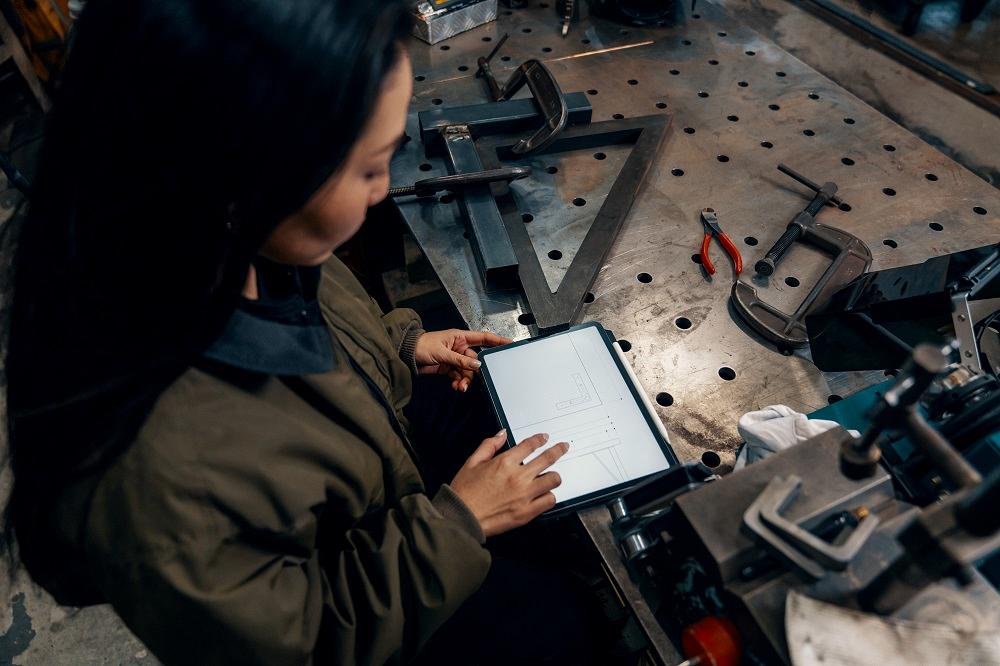 A welder looks at a print on a tablet.