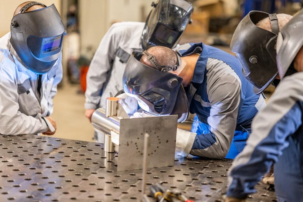 Welding steel parts in workshop. Group of workers standing around workplace. People working in engineering industrial production.