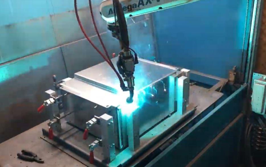 A robotic welder applies a bead to a metal cabinet.