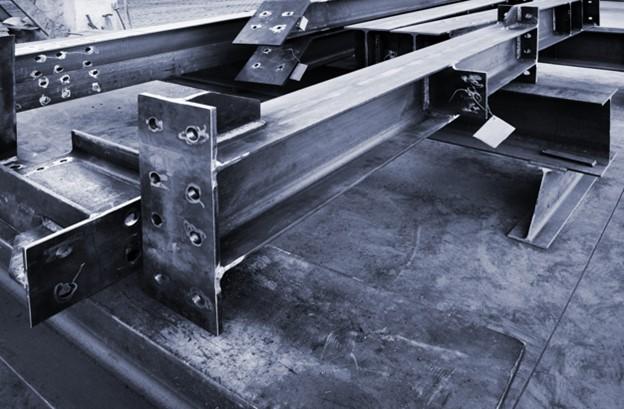 Fabricated structural steel sections are stacked on a shop floor.