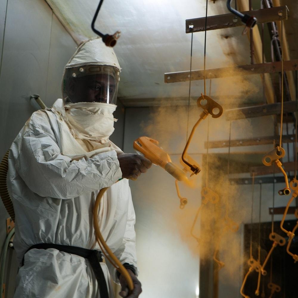 A worker sprays powder coating on a tubular part.