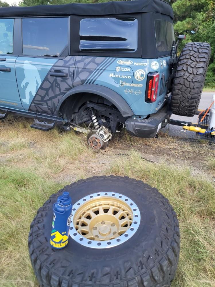 A tire sits in the grass next to the vehicle it came off.