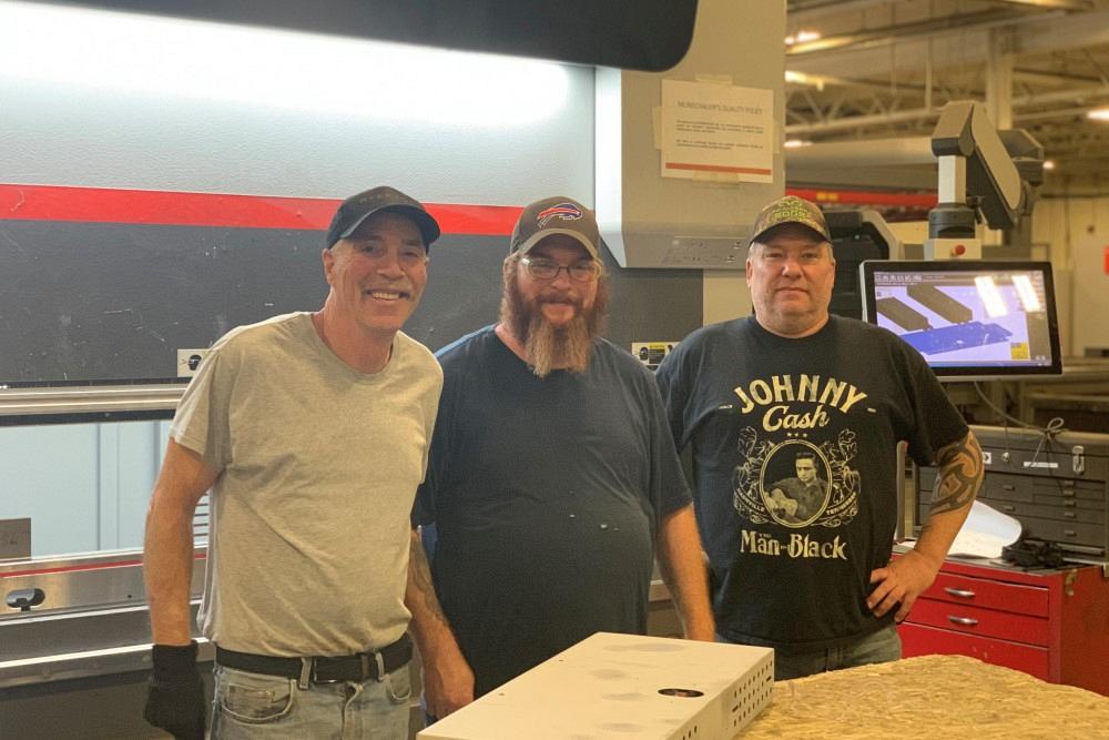 Jim Baer, Jim Baer Jr., and Steve Thompson of ATECH-SEH Metal Fabricators pose in front of a press brake.