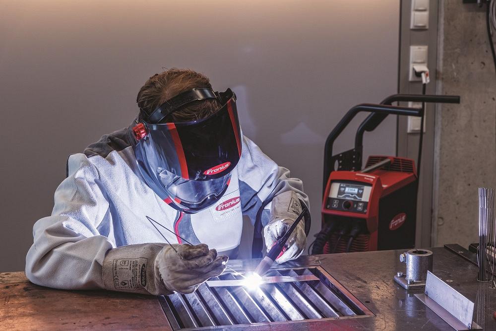Welder wearing a helmet with autodarkening technology to weld a  metal component 